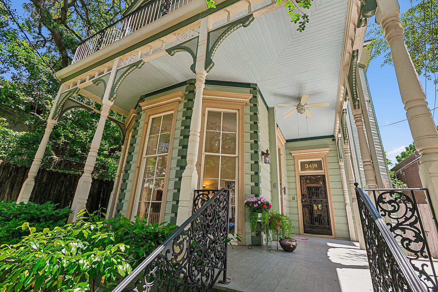 Ornate New Orleans porch with cast-iron railings, gallery columns, and lush greenery