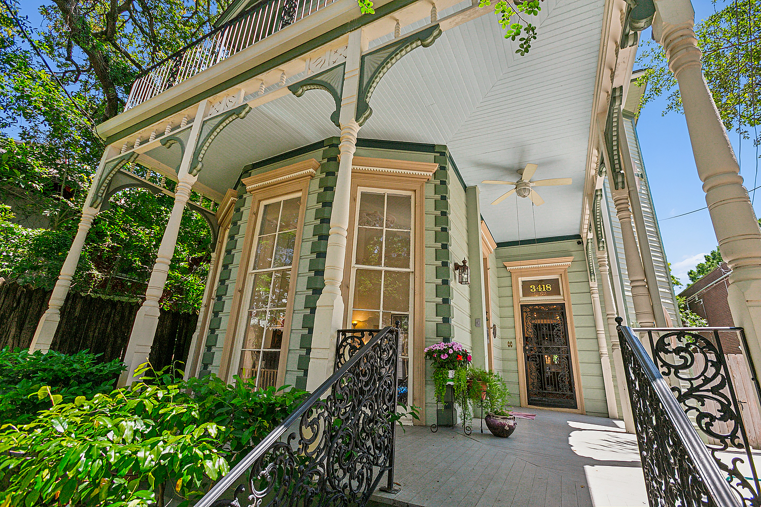 Ornate New Orleans porch with cast-iron railings, gallery columns, and lush greenery